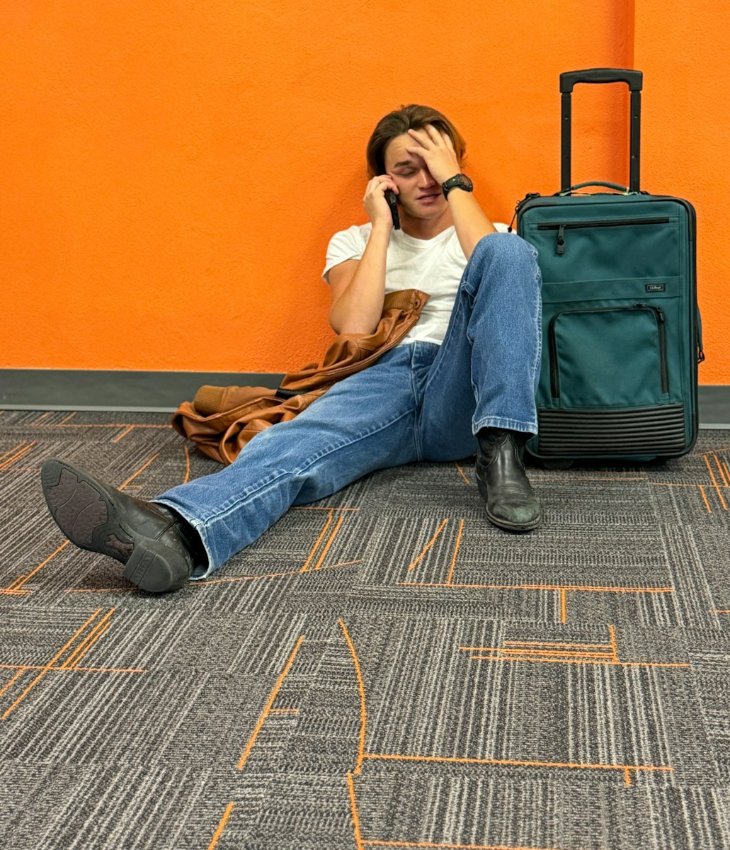 Man sitting on floor with suitcase, looking distressed.
